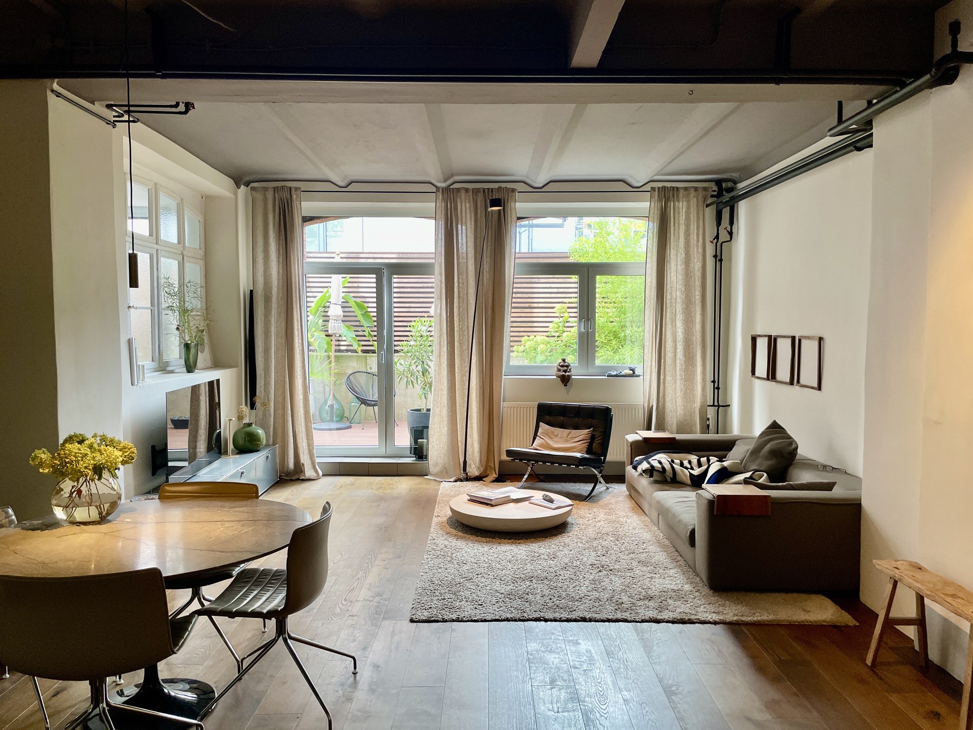 Saniertes Altbau-Wohnzimmer mit Holzbalkendecke, Barcelona-Sessel und Terrassentür