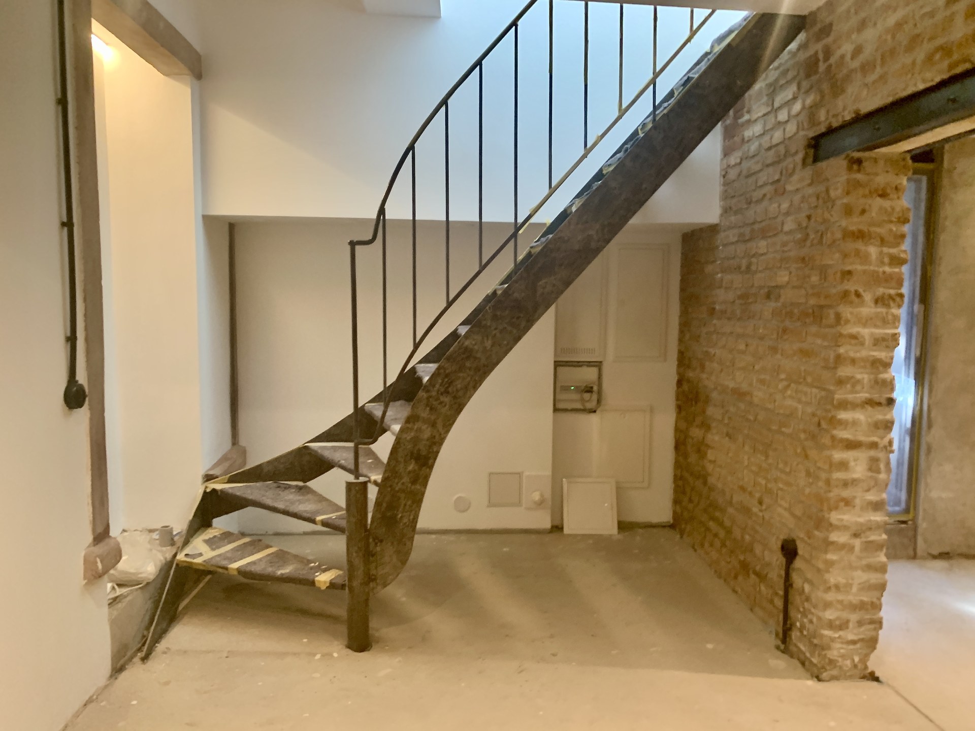 Geschwungene Stahltreppe im Altbau mit Sichtziegelwand im Rohbauzustand